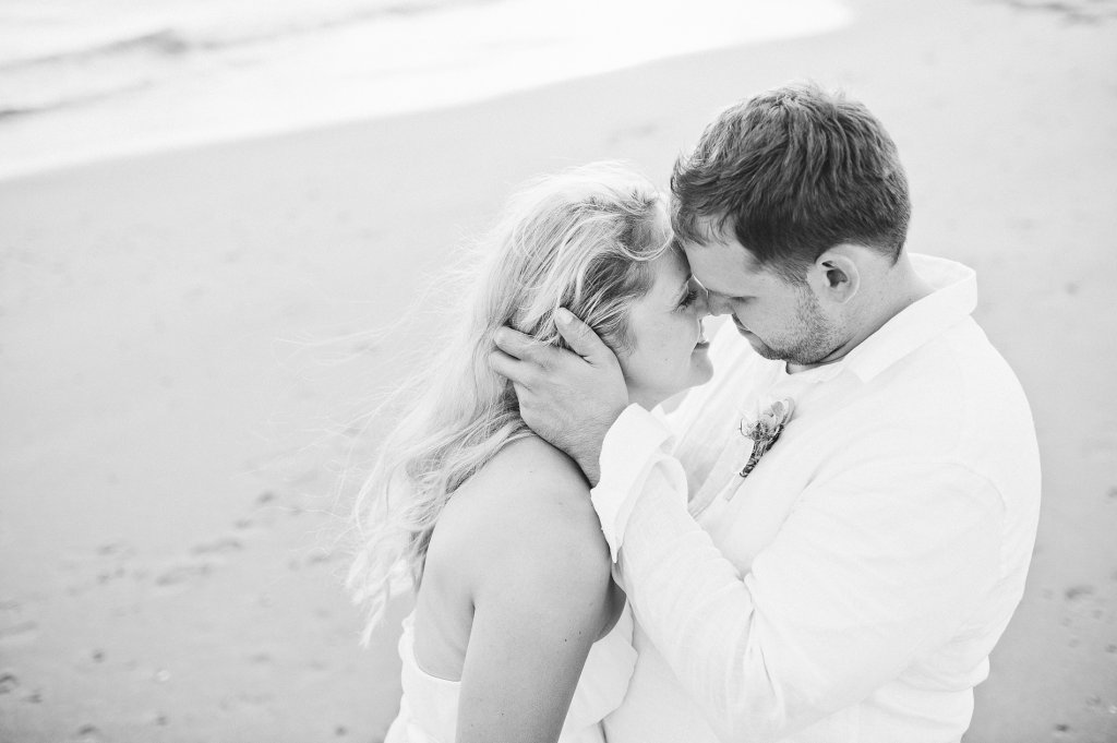 Photo groom holds brides hair gently back, as he attempts to kiss her